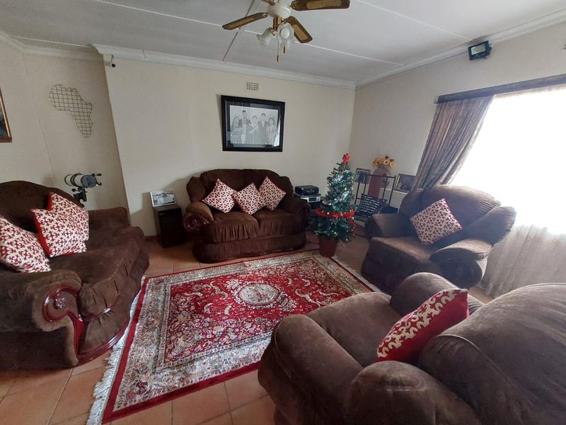 A spacious living room featuring tiled flooring, a ceiling fan, and large windows that provide natural light.