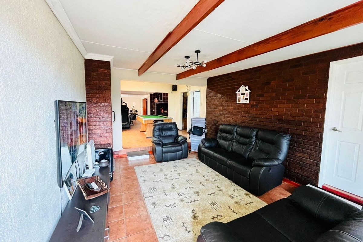 Spacious living area featuring exposed timber ceiling beams and a prominent face-brick feature wall, leading into an adjacent games room.