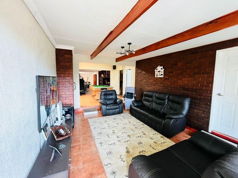 Spacious living area featuring exposed timber ceiling beams and a prominent face-brick feature wall, leading into an adjacent games room.