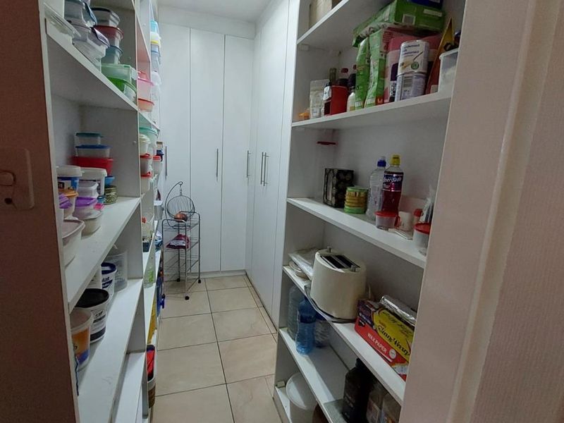 A functional walk-in pantry featuring floor-to-ceiling built-in shelving and tiled flooring, providing ample storage space for kitchen essentials.