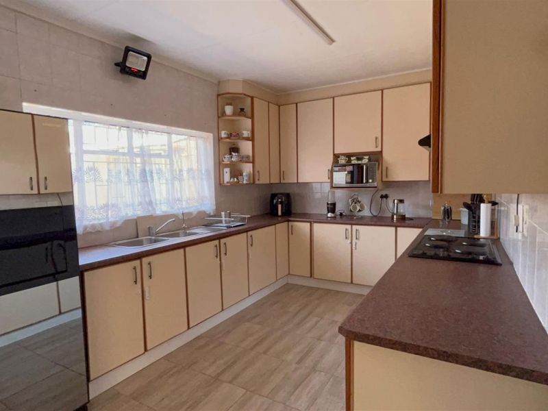 A functional kitchen featuring ample cabinetry, a double sink, built-in hob, and tiled flooring, offering a practical layout for daily meal preparation.
