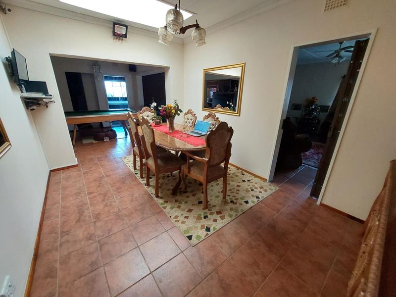A dining room featuring terracotta floor tiles, a central chandelier, and an open-plan layout connecting to an adjacent games area.