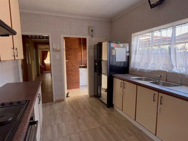 Functional kitchen featuring built-in cabinetry, laminate countertops, integrated hob, and double basin sink with access to adjacent utility area.