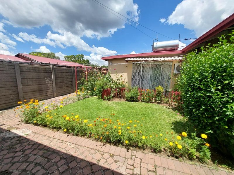 A private rear garden featuring a manicured lawn, flower beds, paved walkway, and a solar water heating system mounted on the roof.
