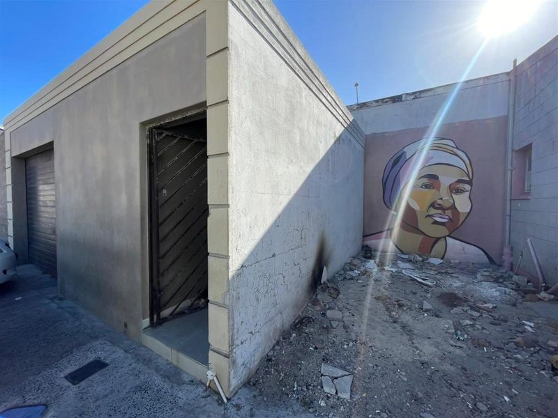 Rear exterior view of a property showing a security gate, concrete structure, and a mural on the adjacent wall with visible debris and surface damage.