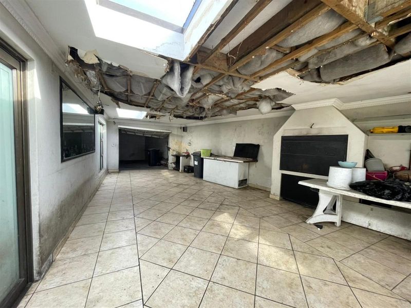 An outdoor patio area featuring a built-in fireplace and skylights, currently requiring significant ceiling repairs and structural maintenance.