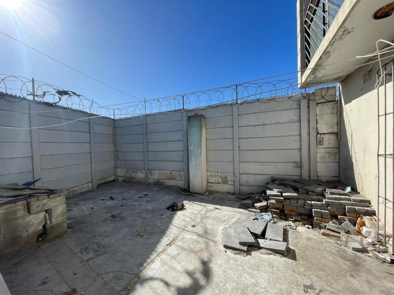 A rear outdoor area featuring a precast concrete boundary wall with security razor wire and a concrete paved surface requiring maintenance and clearing.