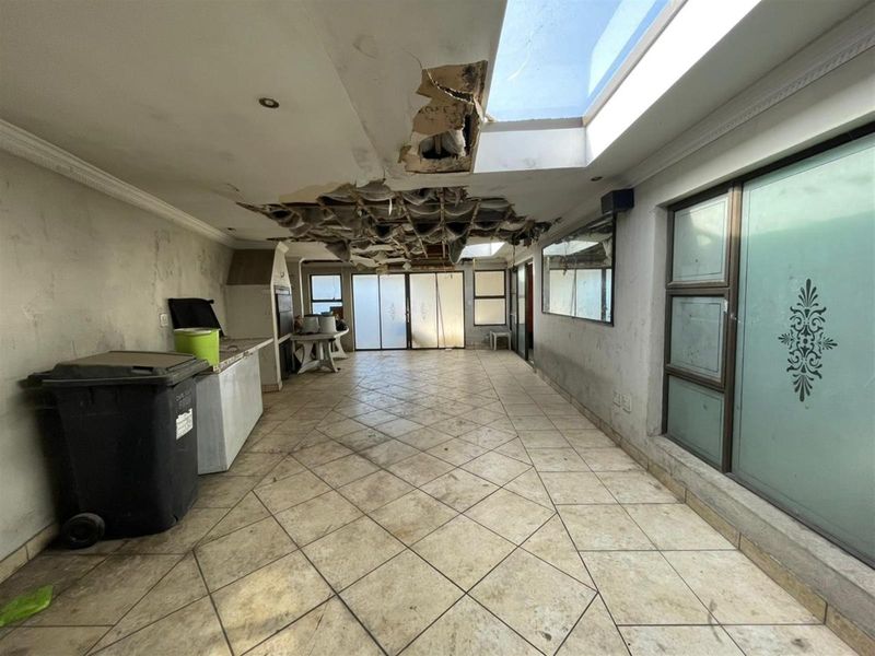 An expansive covered patio area featuring a built-in braai, large skylight, and tiled flooring, currently requiring significant ceiling and wall repairs.