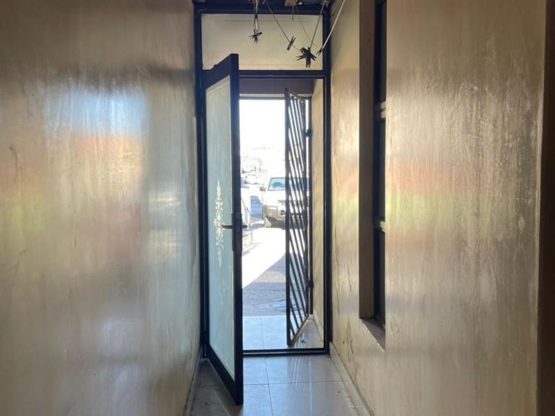 A narrow hallway featuring tiled flooring and a security gate, currently requiring ceiling completion and general cosmetic repairs.