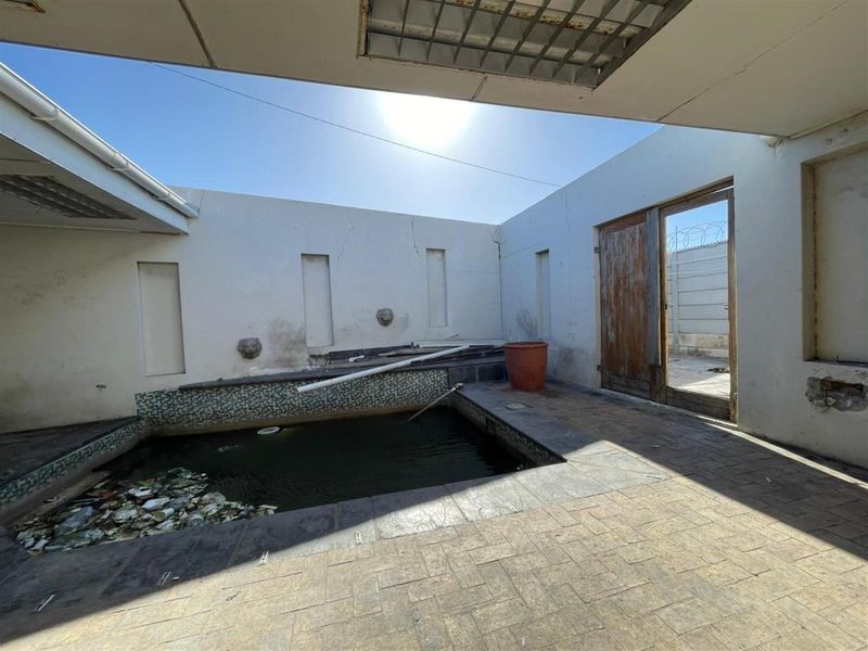 Outdoor pool area featuring a covered patio, tiled flooring, and recessed wall details, currently requiring significant maintenance and repair to restore its condition.