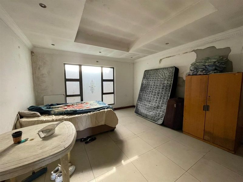 A bedroom featuring tiled flooring and a recessed ceiling, currently requiring significant wall repairs and cosmetic updates to restore its condition.