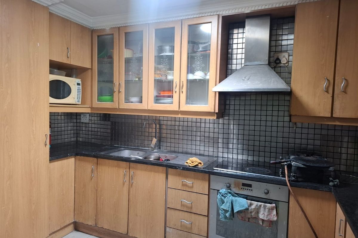A functional kitchen featuring wood-finish cabinetry, dark countertops, a tiled backsplash, and integrated stainless steel appliances including an oven and extractor fan.