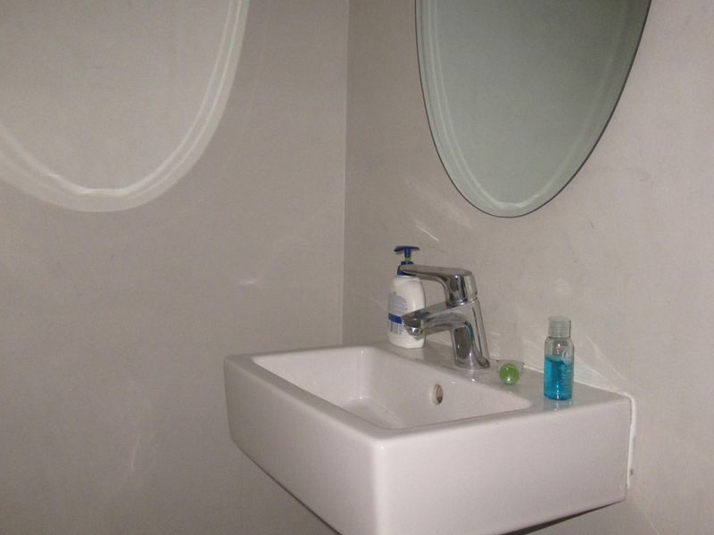 A clean, minimalist bathroom featuring a modern wall-mounted basin with a chrome mixer tap and an oval wall mirror.