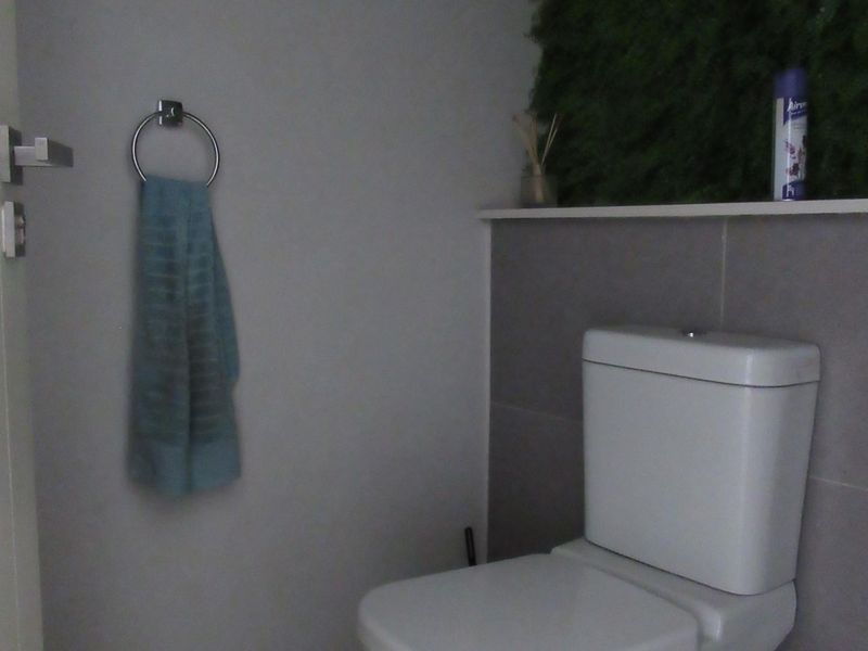 A compact bathroom featuring a modern toilet, tiled wall accents, and a convenient built-in shelf for storage.