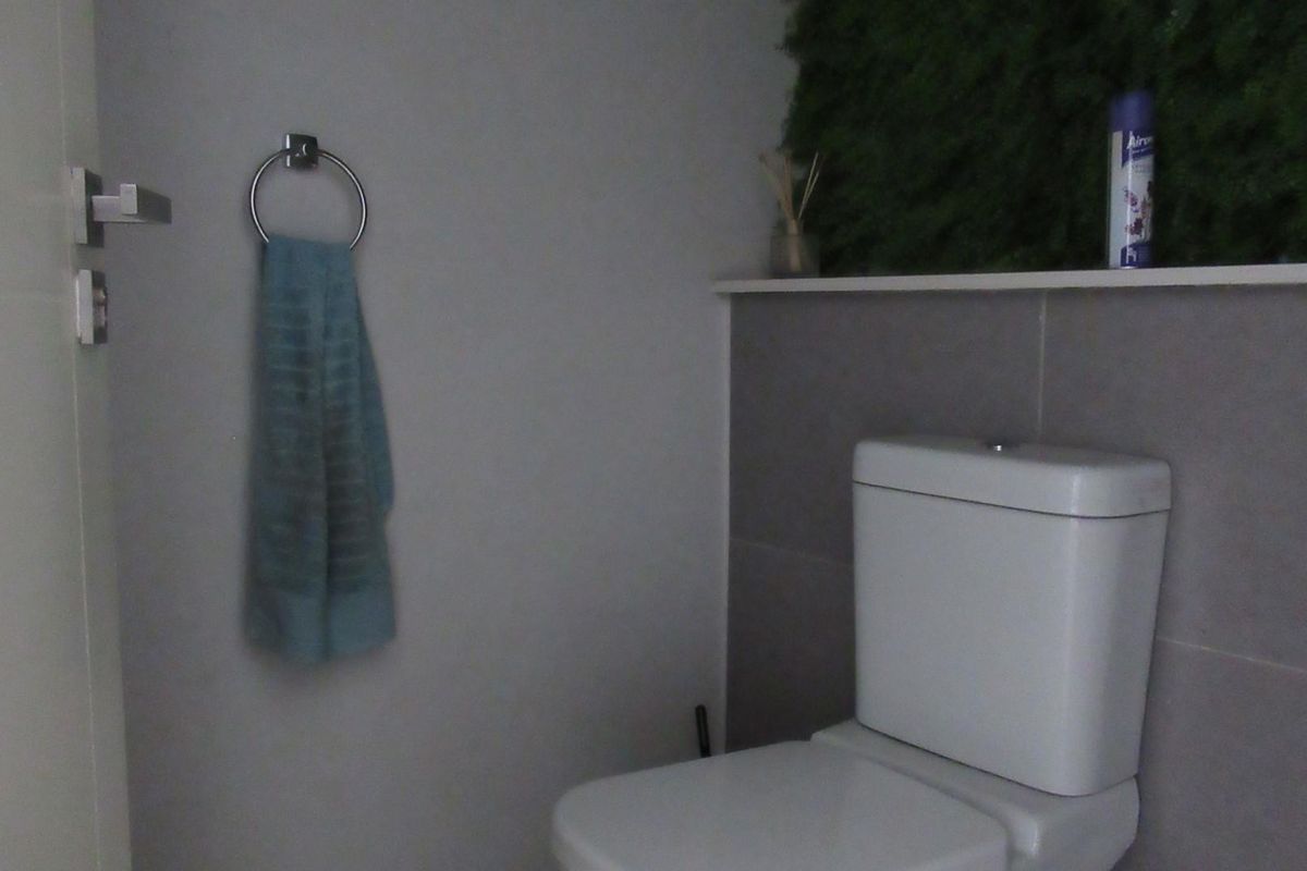 A compact bathroom featuring a modern toilet, tiled wall accents, and a convenient built-in shelf for storage.