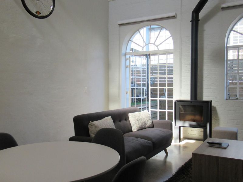 Open plan living area featuring a modern freestanding fireplace, polished concrete floors, and large arched windows providing natural light and access to the patio.