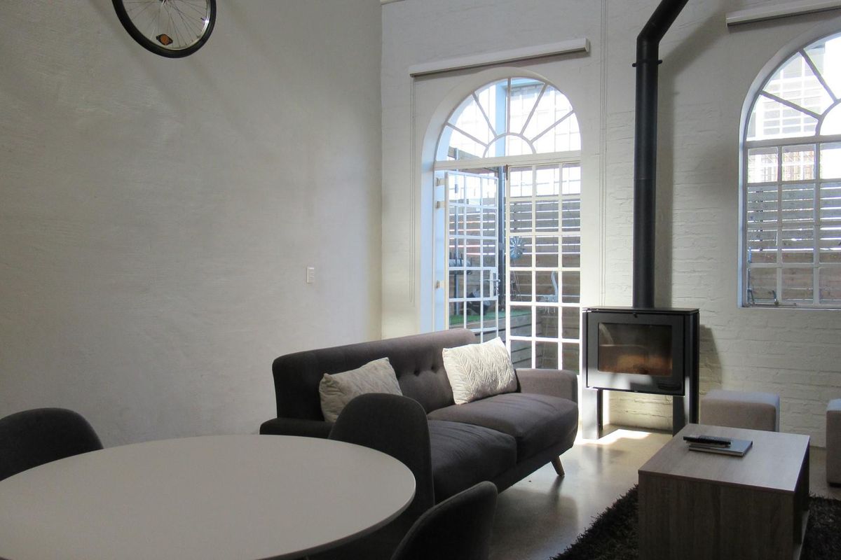 Open plan living area featuring a modern freestanding fireplace, polished concrete floors, and large arched windows providing natural light and access to the patio.