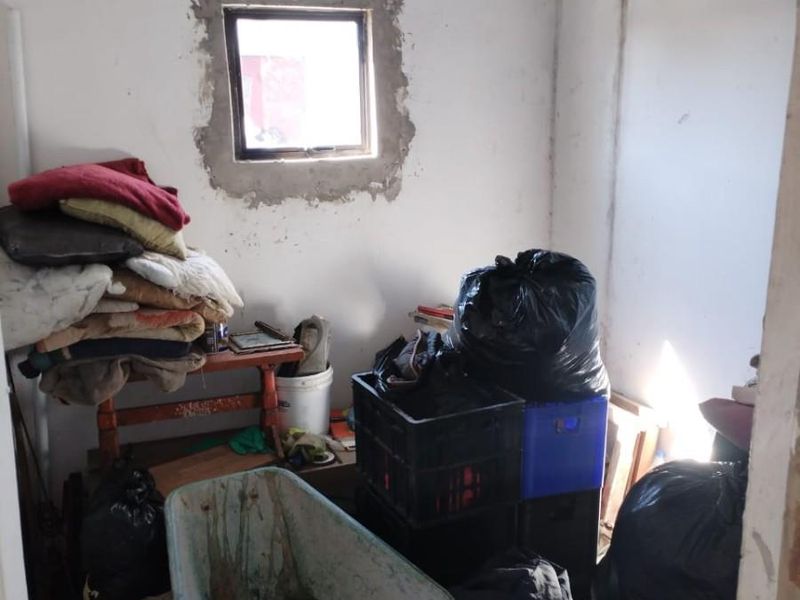 A small utility space featuring unfinished wall plastering and an exposed corrugated metal roof, currently used for storage.