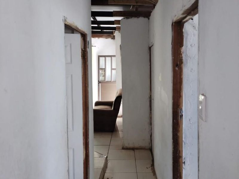 A narrow hallway featuring tiled flooring and an exposed roof structure, requiring significant renovation and finishing to the walls and door frames.