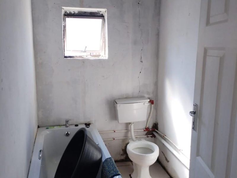 A small, basic bathroom featuring a bathtub and toilet, currently in need of significant renovation and repair to wall and ceiling finishes.