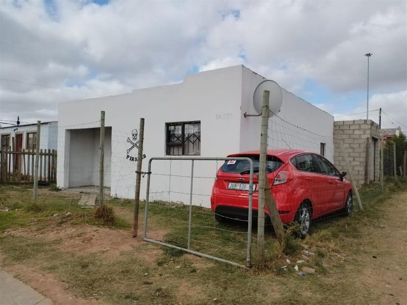 Front exterior view of a single-story residential property featuring a simple facade, security fencing, and a gated entrance.