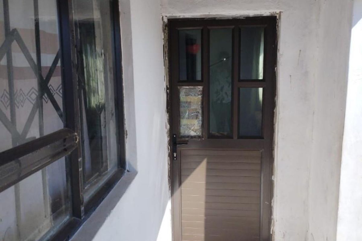 A rear exterior entrance area featuring a brown aluminium door and window, showing significant signs of wear and unfinished plasterwork around the door frame.