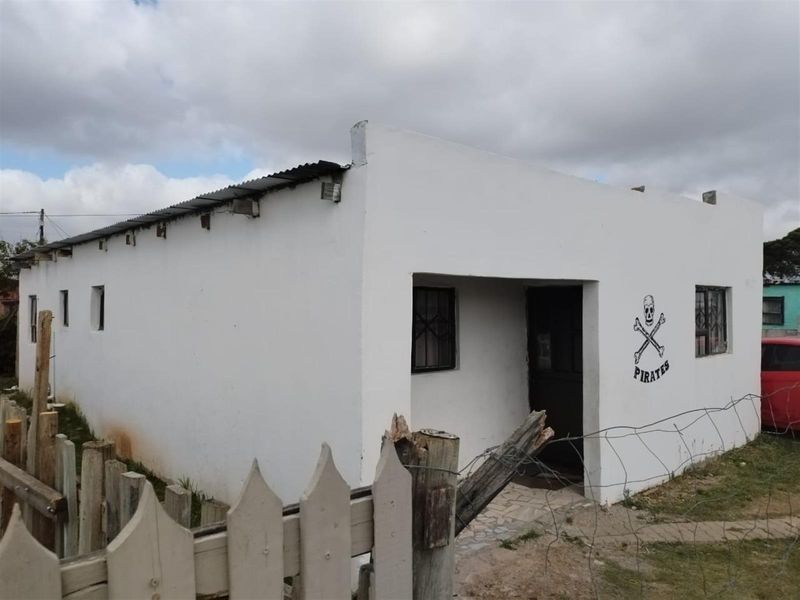Front exterior view of a single-story house featuring a white rendered facade, corrugated metal roof, and security window bars.