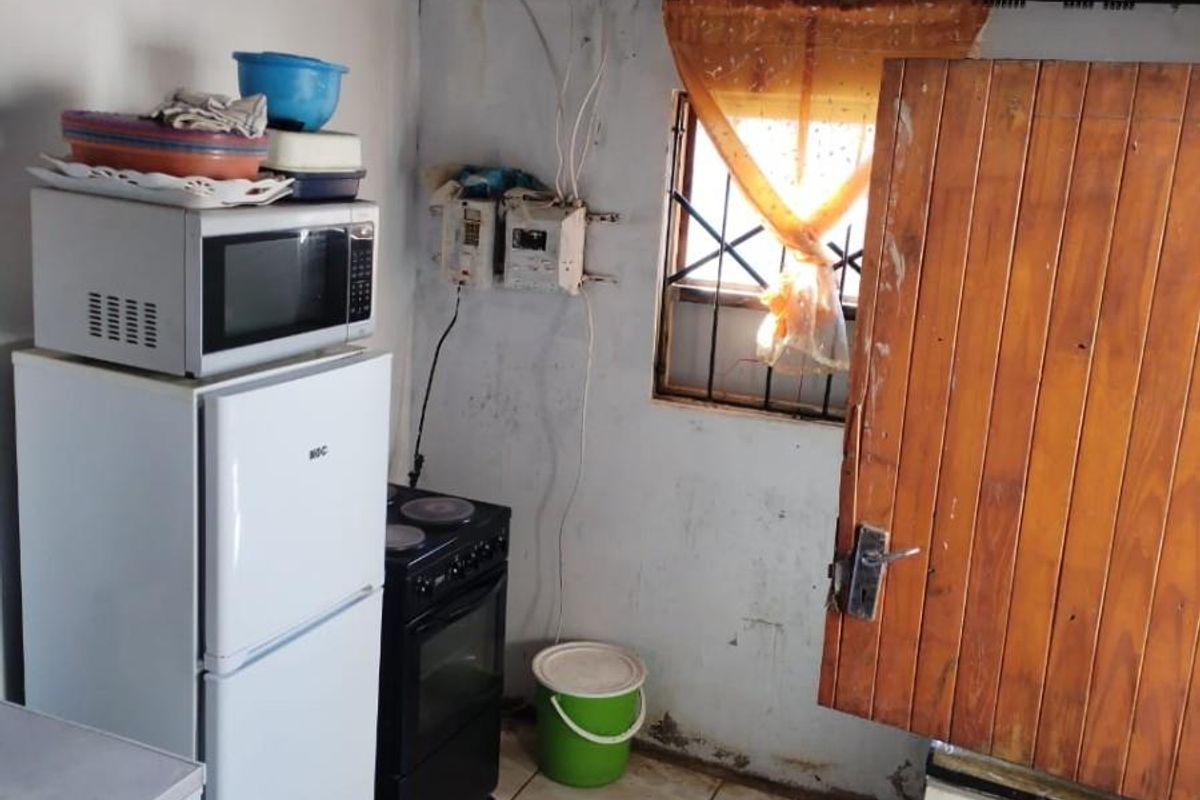 A small, basic kitchen area featuring tiled floors, exposed ceiling beams, and a timber door, currently requiring significant maintenance and cosmetic renovation.