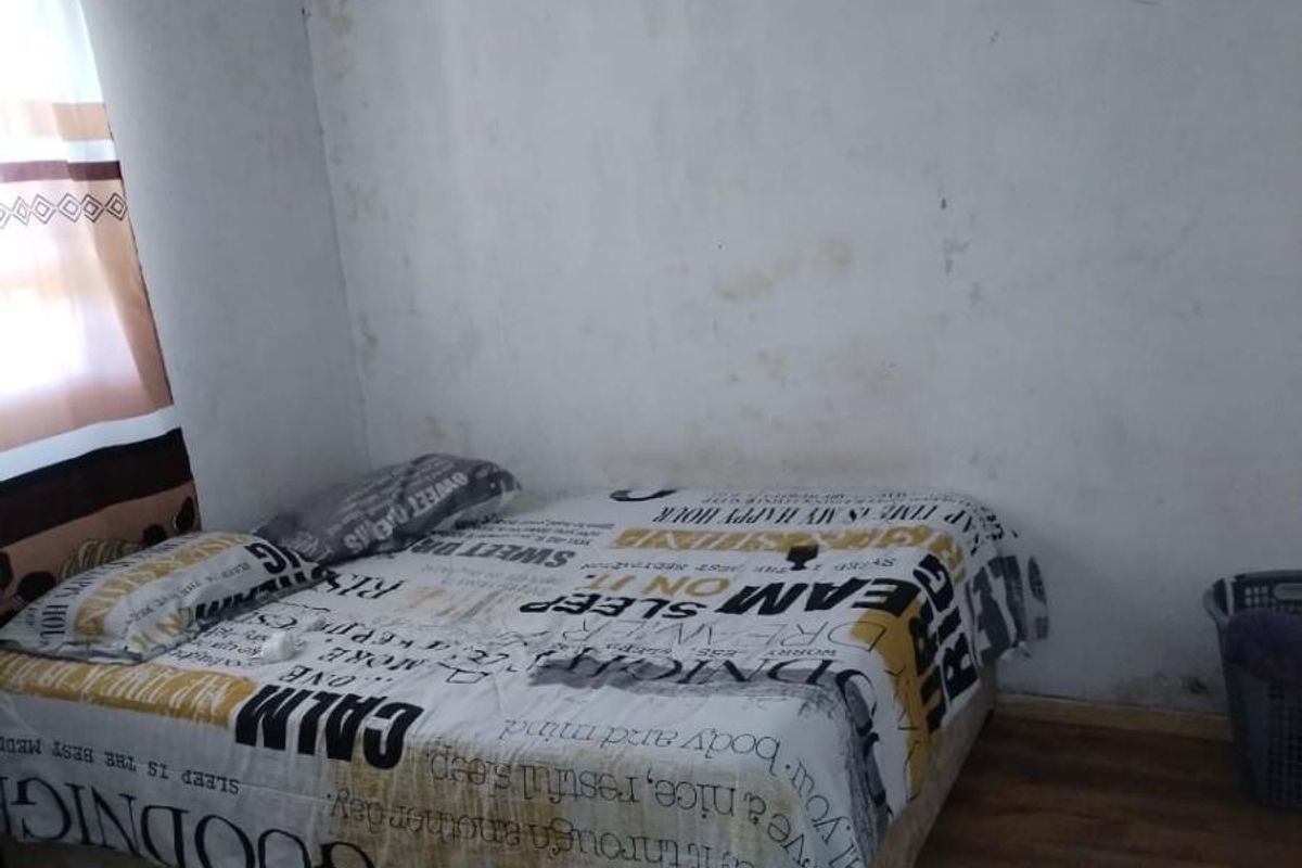 A bedroom featuring laminate flooring and exposed timber roof rafters with a corrugated metal ceiling, requiring wall repairs and cosmetic updates.