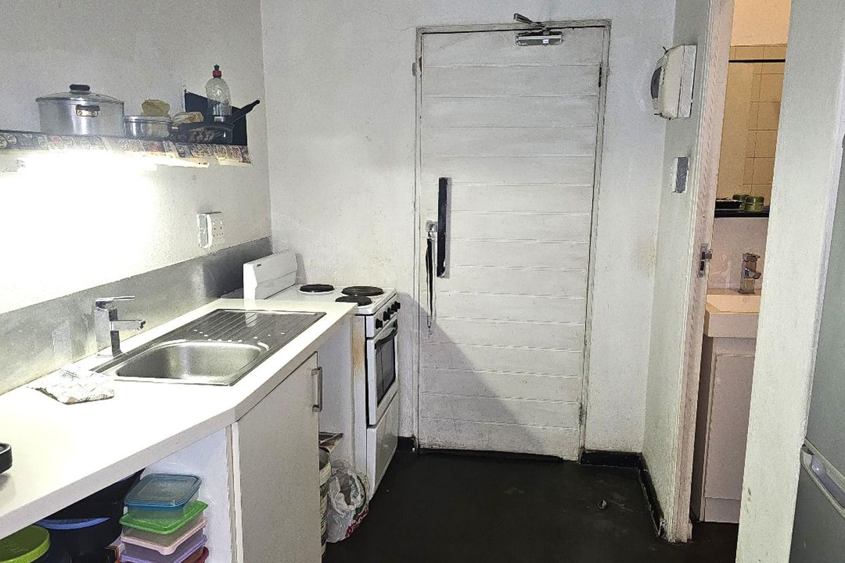 A compact kitchen featuring a stainless steel sink, electric stove, and oven, with direct access to an adjacent bathroom area.