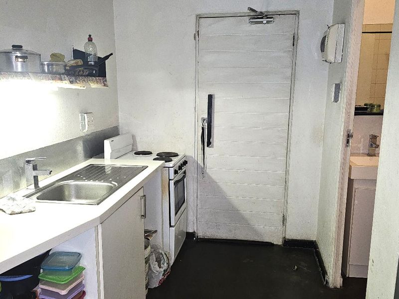 A compact kitchen featuring a stainless steel sink, electric stove, and oven, with direct access to an adjacent bathroom area.