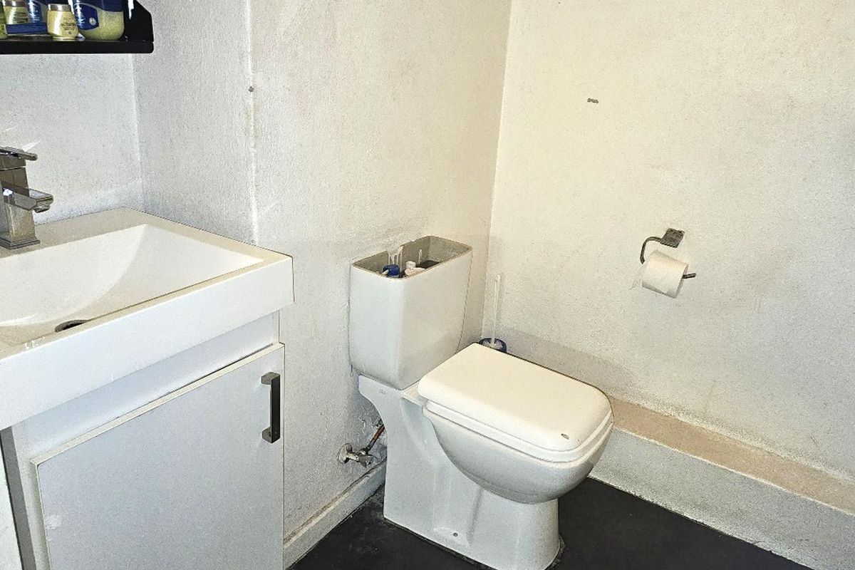 A compact bathroom featuring a vanity with basin and a toilet. The space requires cosmetic updates to the wall finishes and fixtures.