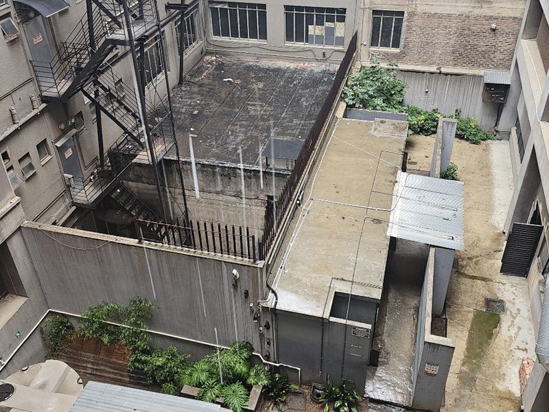 An elevated view of the building's rear courtyard area, featuring concrete surfaces, a fire escape staircase, and industrial-style exterior infrastructure.