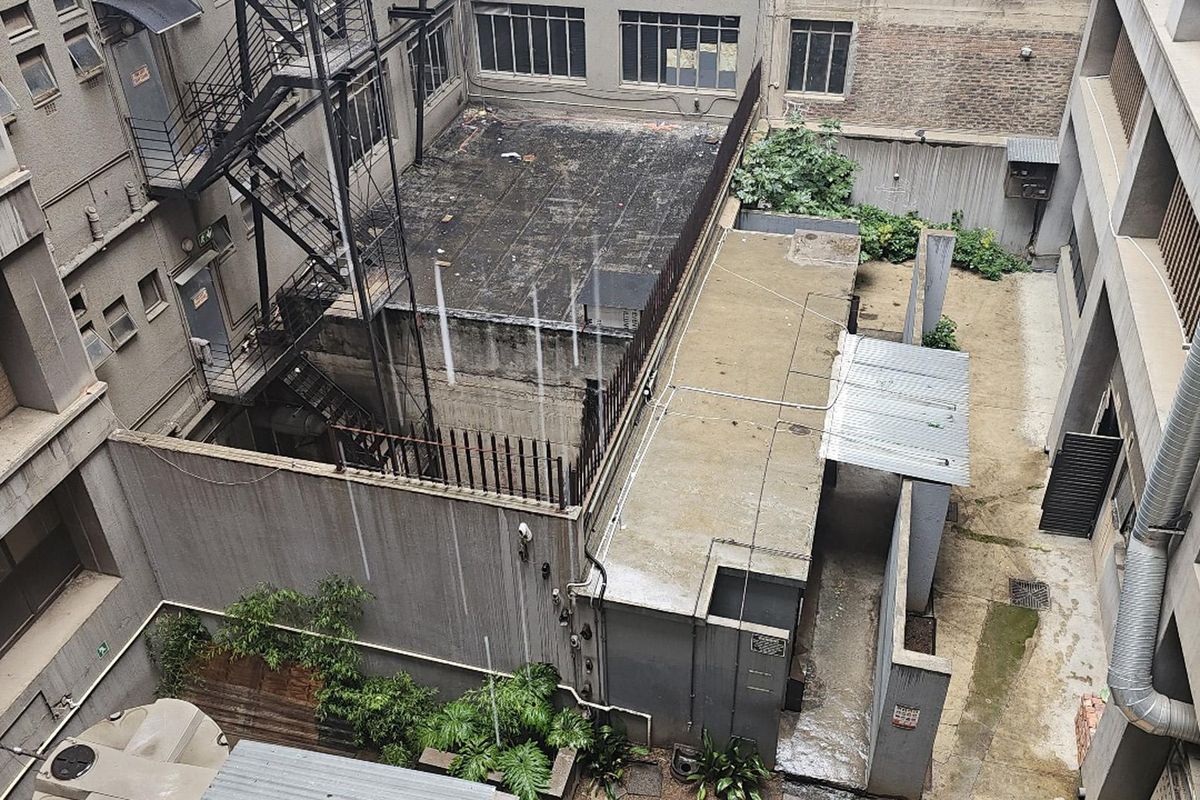 An elevated view of the building's rear courtyard area, featuring concrete surfaces, a fire escape staircase, and industrial-style exterior infrastructure.