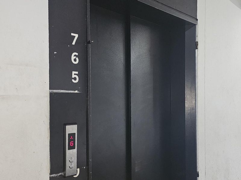 A view of a building elevator in a hallway setting, featuring a black metal door and digital floor indicator.