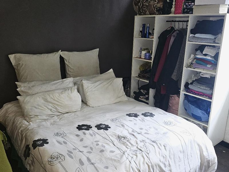 A compact bedroom featuring a dark accent wall and integrated shelving unit, requiring cosmetic updates to improve the overall aesthetic.