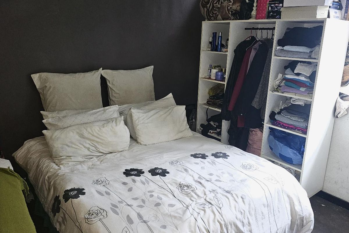 A compact bedroom featuring a dark accent wall and integrated shelving unit, requiring cosmetic updates to improve the overall aesthetic.