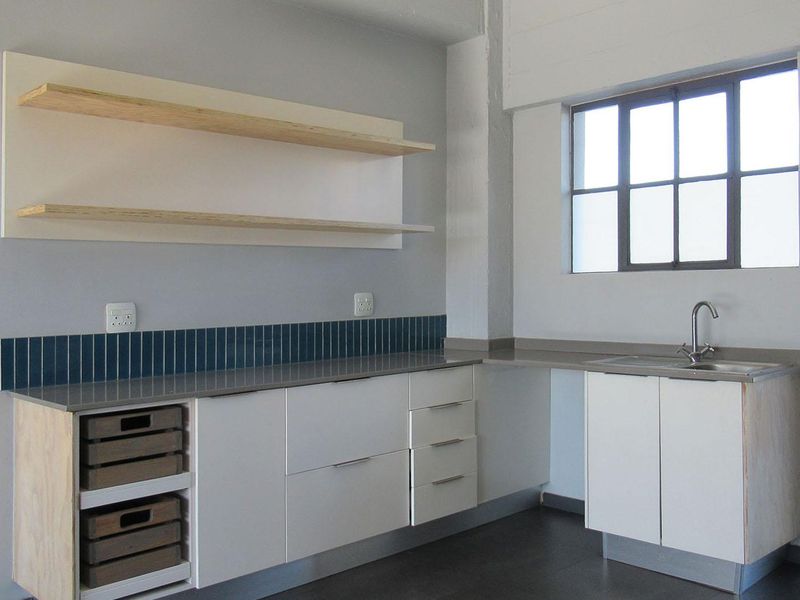 A modern, minimalist kitchen featuring clean white cabinetry, stone countertops, a tiled backsplash, and floating shelves, offering a bright and functional workspace.