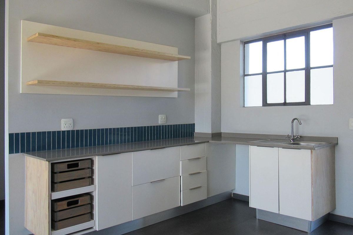 A modern, minimalist kitchen featuring clean white cabinetry, stone countertops, a tiled backsplash, and floating shelves, offering a bright and functional workspace.
