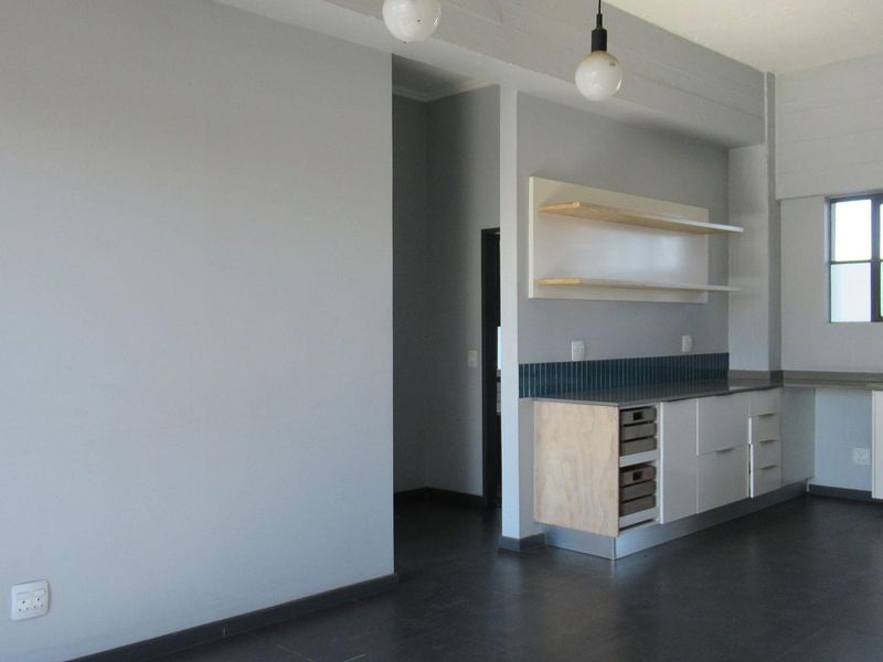 A minimalist kitchen area featuring modern cabinetry, floating shelves, a tiled backsplash, and a sink, set against a neutral grey backdrop.