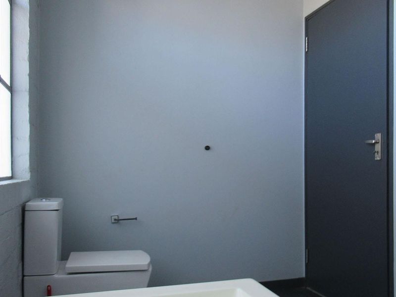 A minimalist bathroom featuring a modern toilet, steel-framed window, and neutral wall finishes, offering a clean and functional space.