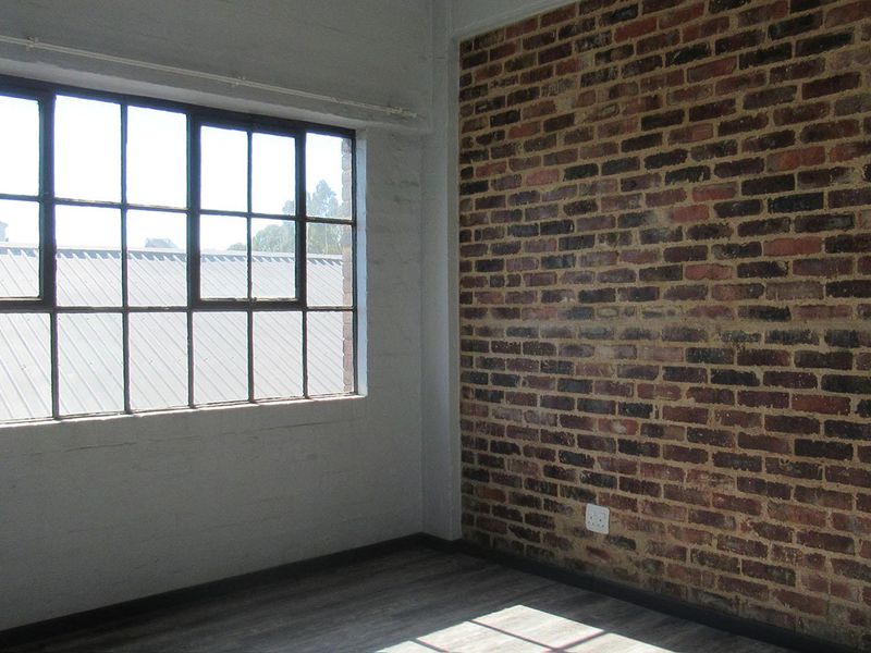 An empty bedroom featuring an industrial-style exposed brick wall, large steel-framed windows, and modern laminate flooring.