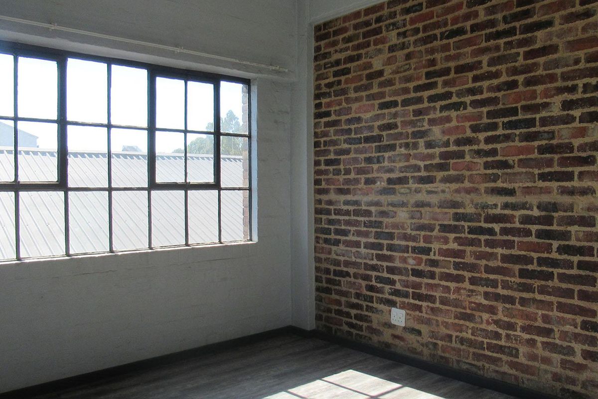 An empty bedroom featuring an industrial-style exposed brick wall, large steel-framed windows, and modern laminate flooring.