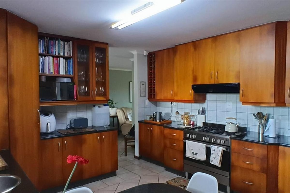A functional kitchen featuring timber cabinetry, dark countertops, tiled splashbacks, and a built-in gas stove with an extractor fan.