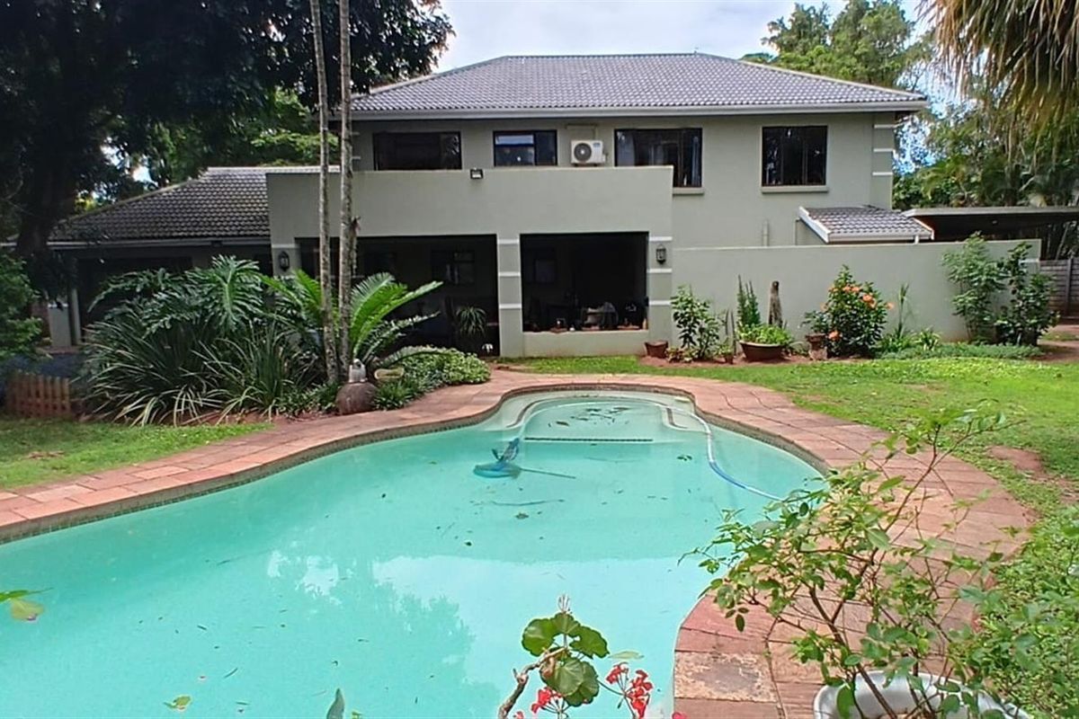 Rear view of the property featuring a swimming pool, landscaped garden, and a two-story house with a tiled roof and covered patio area.