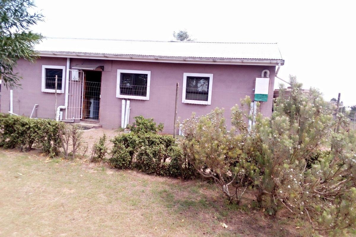 A view of the rear exterior of the farm dwelling, featuring a simple facade, metal roof, and surrounding garden area.