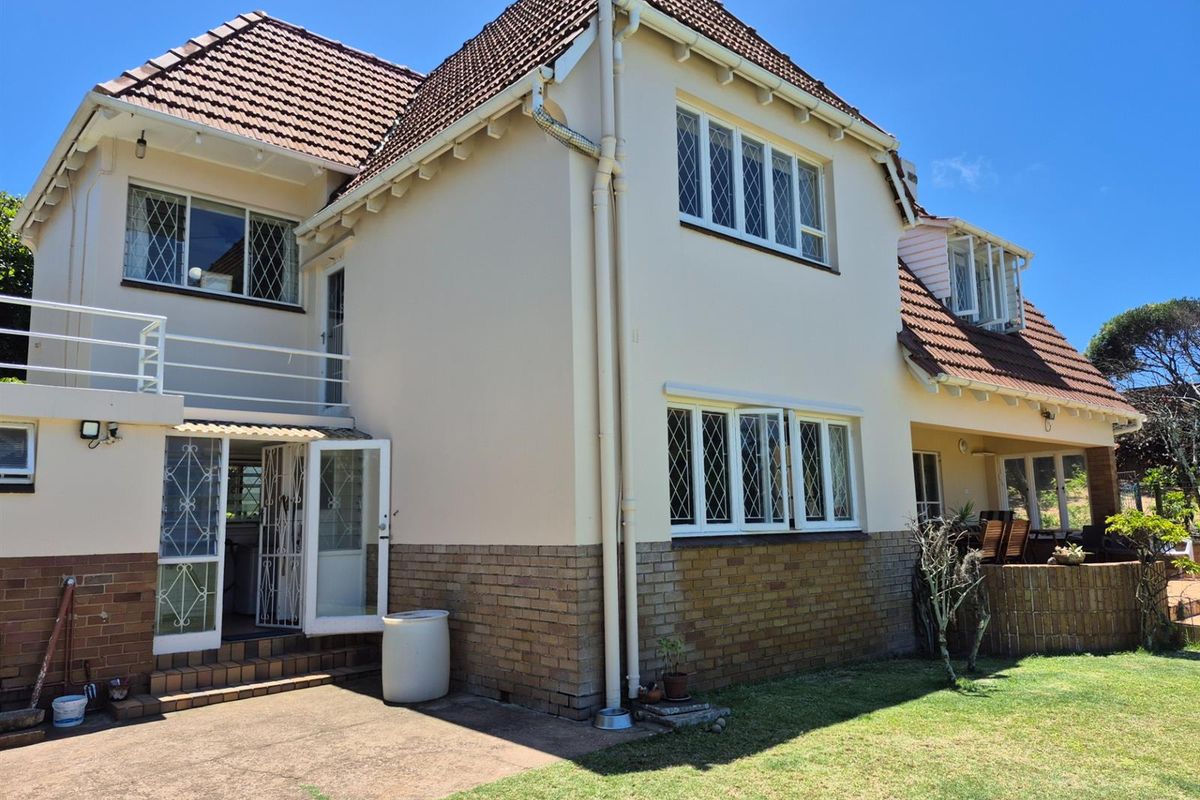 Rear view of a multi-story residence featuring a tiled roof, brick base, and a raised balcony area overlooking the garden.