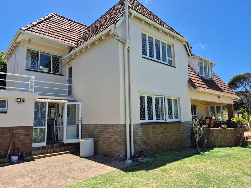 Rear view of a multi-story residence featuring a tiled roof, brick base, and a raised balcony area overlooking the garden.