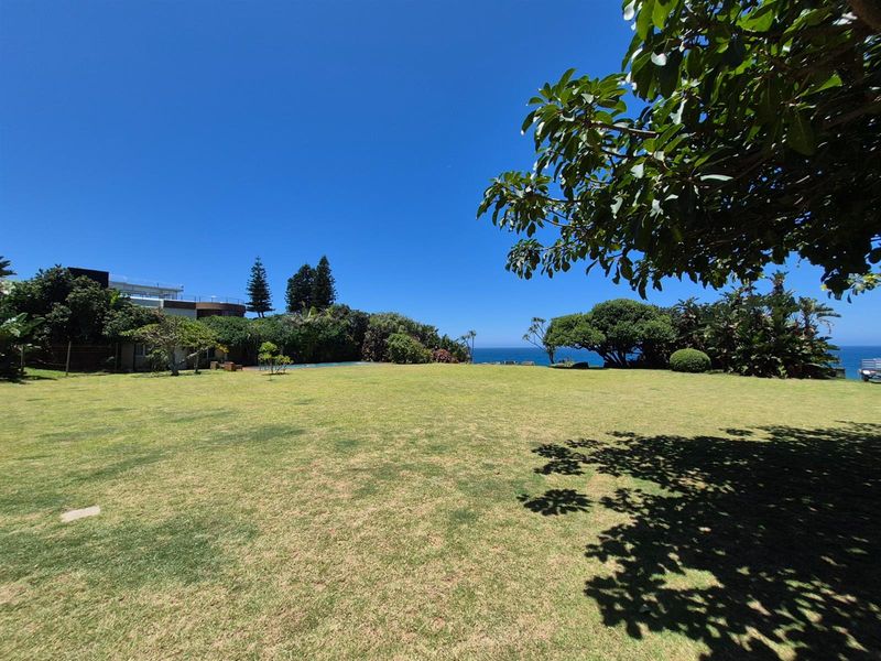 Expansive, well-maintained lawn area featuring mature trees and a scenic ocean view, providing a peaceful outdoor setting for the property.