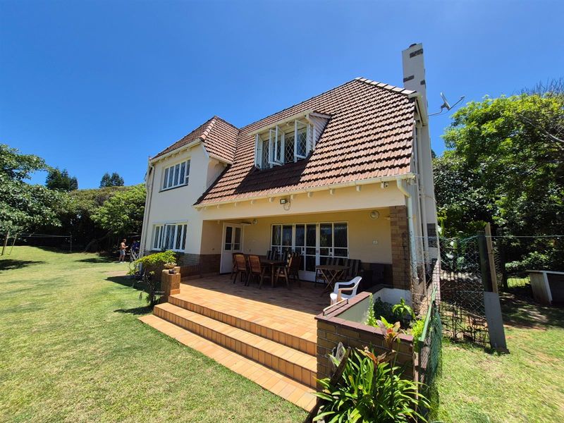 A rear view of the double-story residence featuring a tiled patio, brick staircase, and a spacious garden area.
